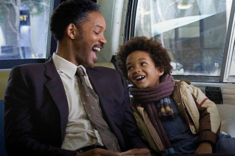 un uomo di colore che, con a fianco suo figlio, ridono mentre sono seduti in un bus.